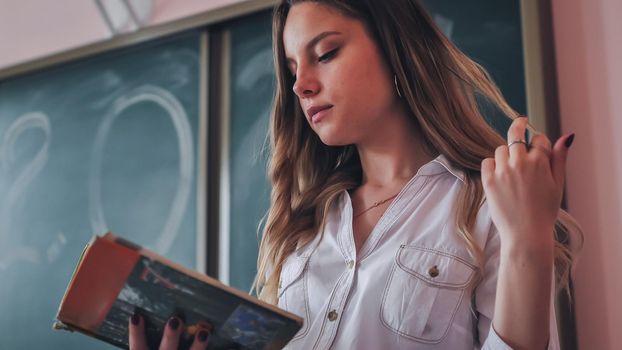 Cute schoolgirl reads a book in class