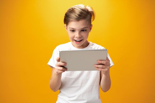 Little boy playing with digital tablet against yellow background, close up