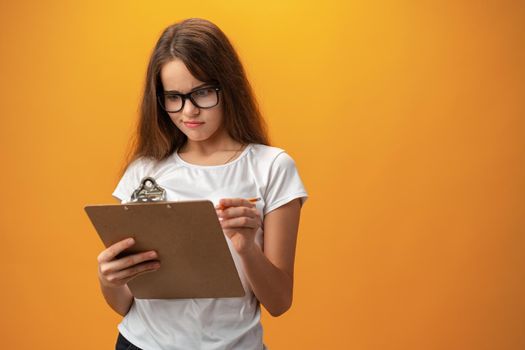 Teen school girl taking notes on clipboard against yellow background, close up