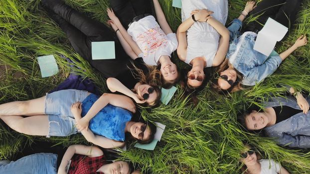 Girls students lie on the grass in a city park with notebooks