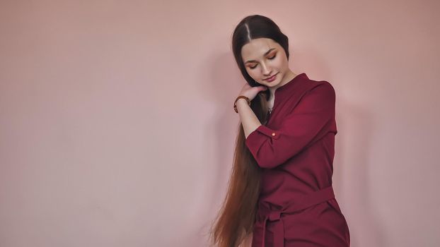 Long-haired girl combs her hair on a pink background