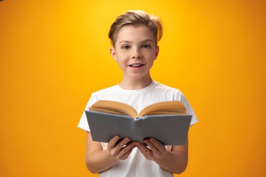 Little schoolboy holding a book against yellow background, close up
