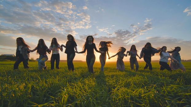 A group of girls walk towards the sun at sunset holding hands