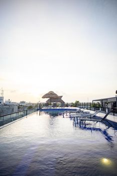 Beautiful view of umbrellas and shallow pool with beach beds in hotel under bright sky. Peaceful view of white skyline above tropical resort rooftop. Holidays and landscapes