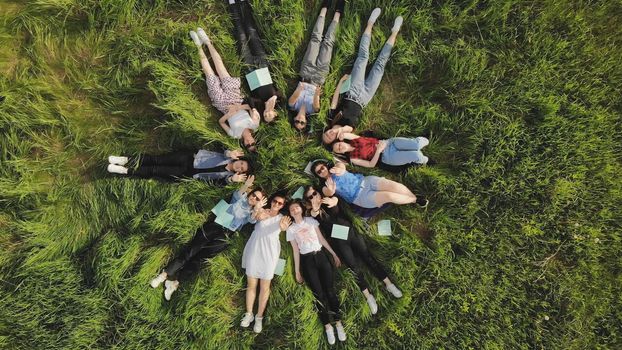 Girls students lie on the grass in a city park with notebooks