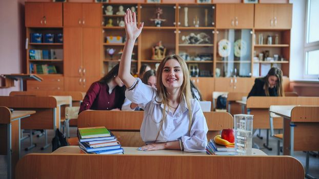 A girl student sitting at a desk raises her hand in the class