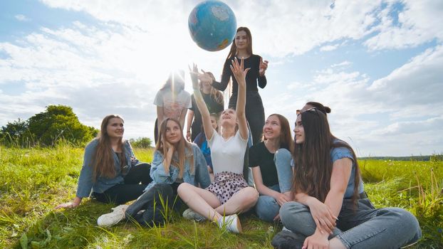 A group of girls students sit in the meadow and toss the world globe up
