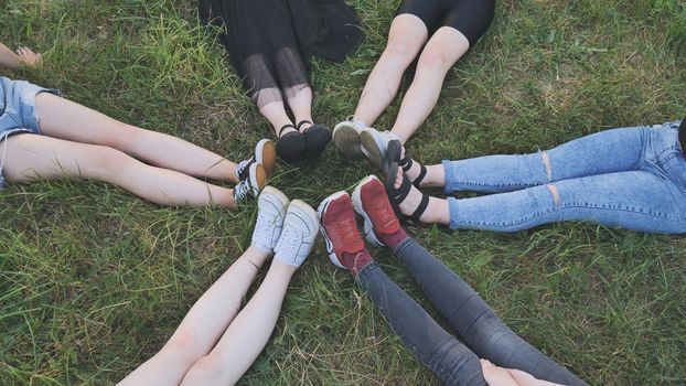 Friends are sitting on the grass with their legs joined in a circle