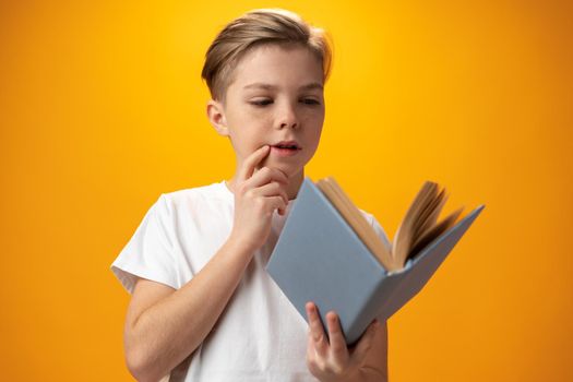 Little schoolboy holding a book against yellow background, close up
