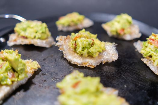 Close-up of delicious pork rinds with guacamole on traditional comal. Tasty avocado sauce on fried pork snacks above round griddle. Authentic Mexican food