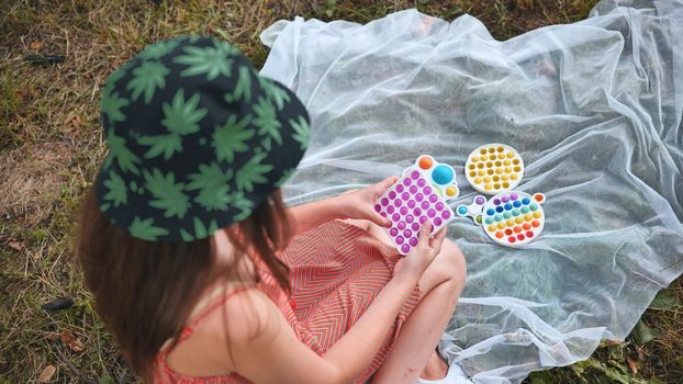 Teen girl plays with anti-stress popit and simple dimple toys in the park on a summer day