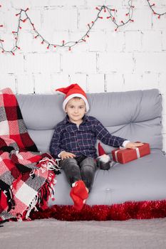 little boy in santa hat near christmas gnome toy, holding toy in hand in grey room. christmas decor and toys. kids playing.