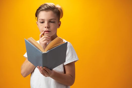 Little schoolboy holding a book against yellow background, close up