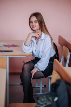 A young charming student is sitting at a school desk