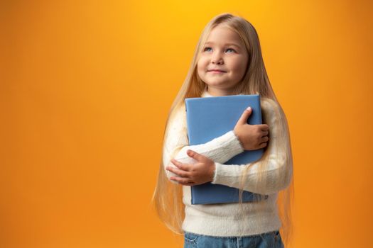 Little beautiful smiling girl holding book against yellow background, close up