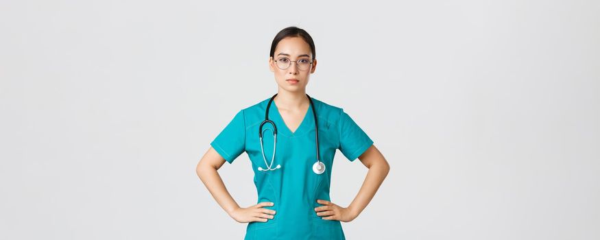 Covid-19, healthcare workers, pandemic concept. Confident determined asian female nurse helping patients, working with coronavirus disease, looking ready, wearing scrubs and glasses, white background.