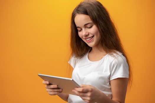 Beautiful teen girl using digital tablet over yellow studio background, close up