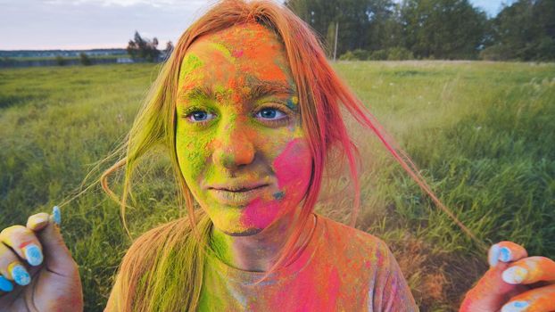 Cheerful girl posing smeared in multi-colored powder. Close-up face