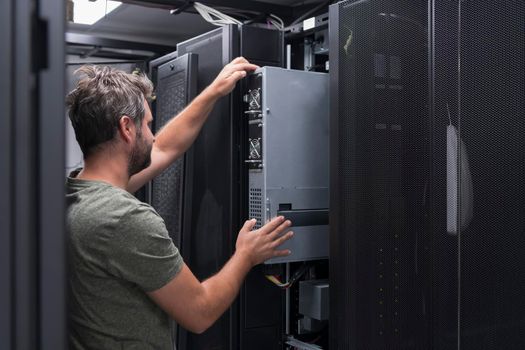 IT engineer working In the server room or data center. The technician puts in a rack a new server of corporate business mainframe supercomputer or cryptocurrency mining farm.