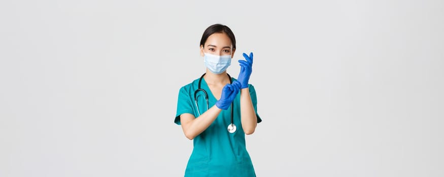 Covid-19, coronavirus disease, healthcare workers concept. Professional and confident smiling asian physician, nurse wear rubber gloves and medical mask for patient examination, white background.