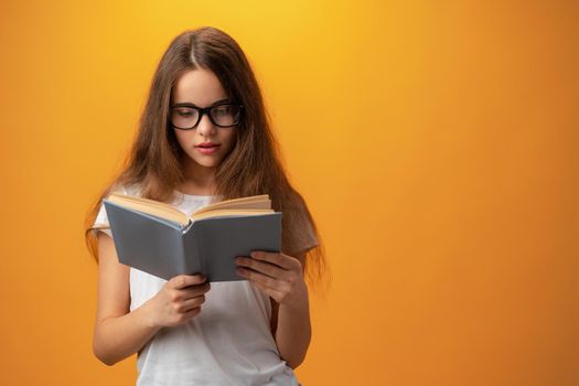 Smart teen girl in glasses holding book against yellow background, close up