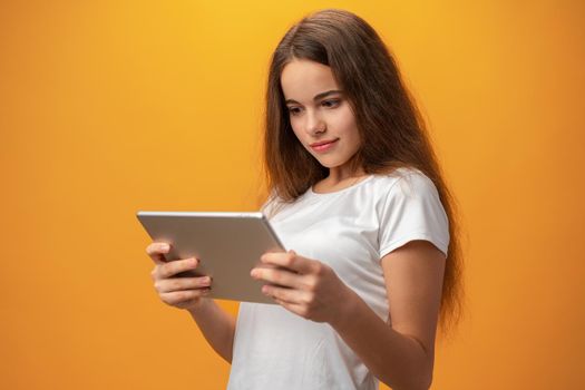 Beautiful teen girl using digital tablet over yellow studio background, close up