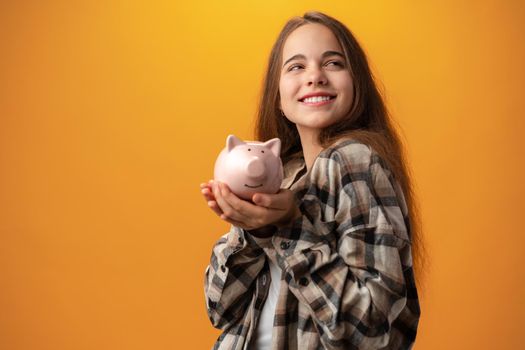 Teen girl with piggy bank on yellow background, close up