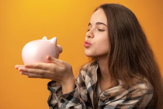 Teen girl with piggy bank on yellow background, close up
