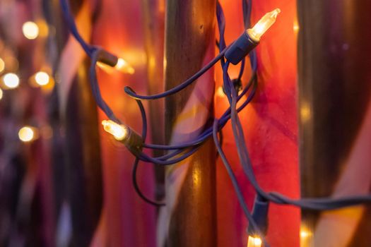 Close-up of little yellow lights hanging in front of two tubes and red wall. Warm Christmas lights decorating interior of room with dim illumination. Decoration and lighting