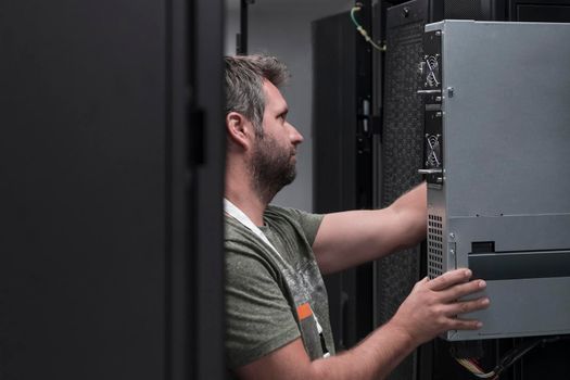 IT engineer working In the server room or data center. The technician puts in a rack a new server of corporate business mainframe supercomputer or cryptocurrency mining farm.