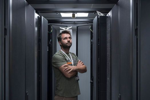 Portrait of male technician or network administrator standing brave as a hero with arms crossed in data center server room. High quality photo