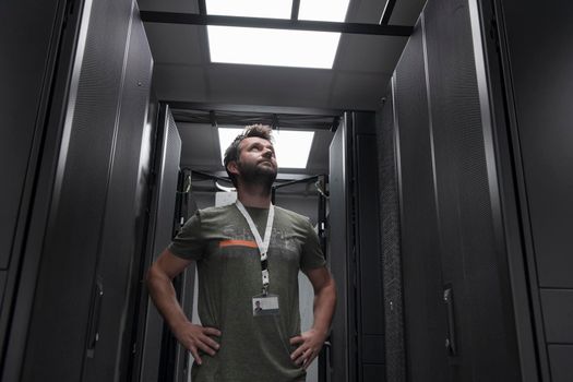 Portrait of male technician or network administrator standing brave as a hero with arms crossed in data center server room. High quality photo