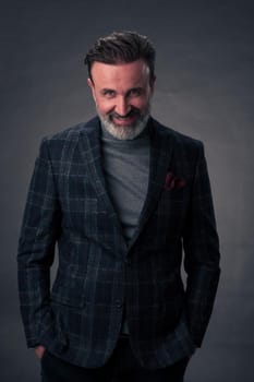 Portrait of a stylish elegant senior businessman with a beard and casual business clothes in photo studio isolated on dark background gesturing with hands. High quality photo