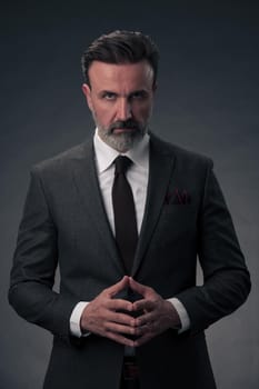 Portrait of a stylish elegant senior businessman with a beard and casual business clothes in photo studio isolated on dark background gesturing with hands. High quality photo