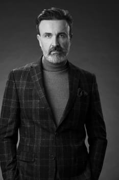 Portrait of a stylish elegant senior businessman with a beard and casual business clothes in photo studio isolated on dark background gesturing with hands. High quality photo