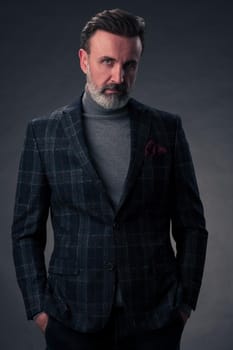 Portrait of a stylish elegant senior businessman with a beard and casual business clothes in photo studio isolated on dark background gesturing with hands. High quality photo