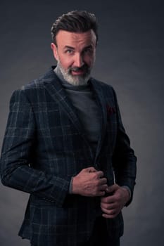 Portrait of a stylish elegant senior businessman with a beard and casual business clothes in photo studio isolated on dark background gesturing with hands. High quality photo