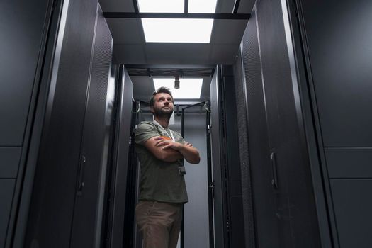 Portrait of male technician or network administrator standing brave as a hero with arms crossed in data center server room. High quality photo