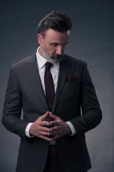 Portrait of a stylish elegant senior businessman with a beard and casual business clothes in photo studio isolated on dark background gesturing with hands. High quality photo