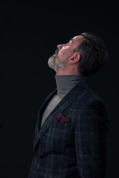 Portrait of a stylish elegant senior businessman with a beard and casual business clothes in photo studio isolated on dark background gesturing with hands. High quality photo