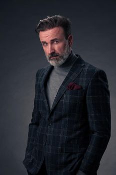 Portrait of a stylish elegant senior businessman with a beard and casual business clothes in photo studio isolated on dark background gesturing with hands. High quality photo