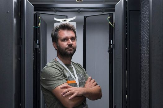 Portrait of male technician or network administrator standing brave as a hero with arms crossed in data center server room. High quality photo