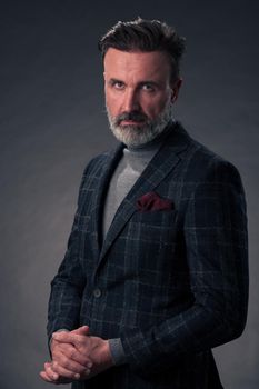 Portrait of a stylish elegant senior businessman with a beard and casual business clothes in photo studio isolated on dark background gesturing with hands. High quality photo