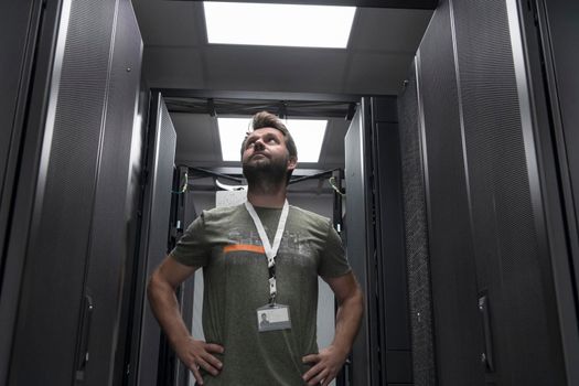 Portrait of male technician or network administrator standing brave as a hero with arms crossed in data center server room. High quality photo