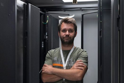 Portrait of male technician or network administrator standing brave as a hero with arms crossed in data center server room. High quality photo