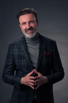 Portrait of a stylish elegant senior businessman with a beard and casual business clothes in photo studio isolated on dark background gesturing with hands. High quality photo