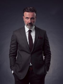 Portrait of a stylish elegant senior businessman with a beard and casual business clothes in photo studio isolated on dark background gesturing with hands. High quality photo