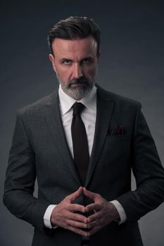 Portrait of a stylish elegant senior businessman with a beard and casual business clothes in photo studio isolated on dark background gesturing with hands. High quality photo