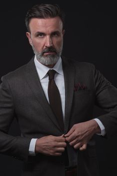 Portrait of adult businessman wearing trendy suit and sitting in modern studio on stylish chair against the black background. Horizontal mockup. High quality photo