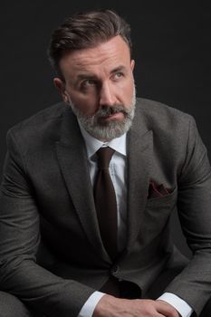 Portrait of adult businessman wearing trendy suit and sitting in modern studio on stylish chair against the black background. Horizontal mockup. High quality photo